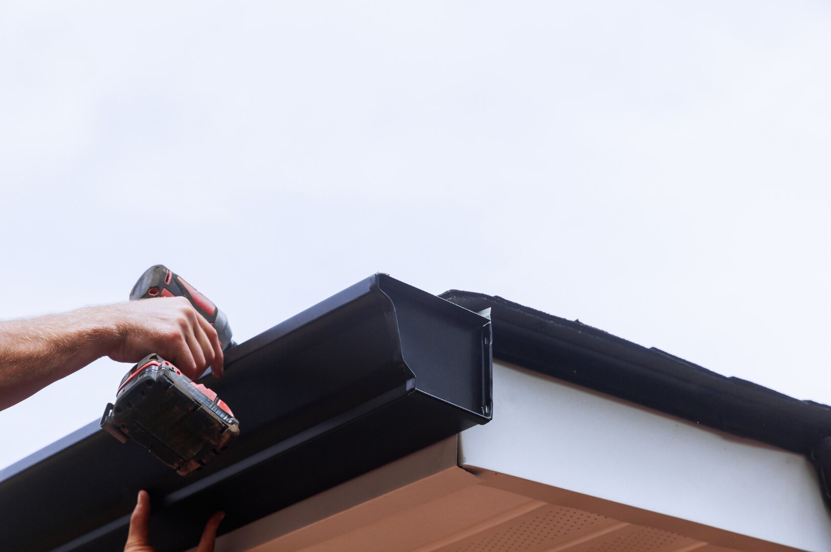 Installer fastening a dark gutter at the roof edge