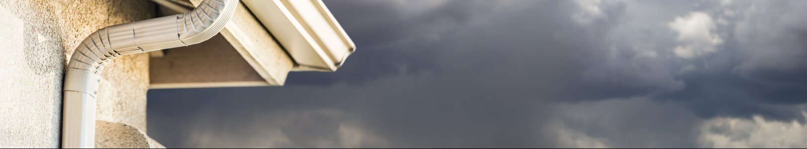 Residential gutter and downpipe beneath a cloudy sky