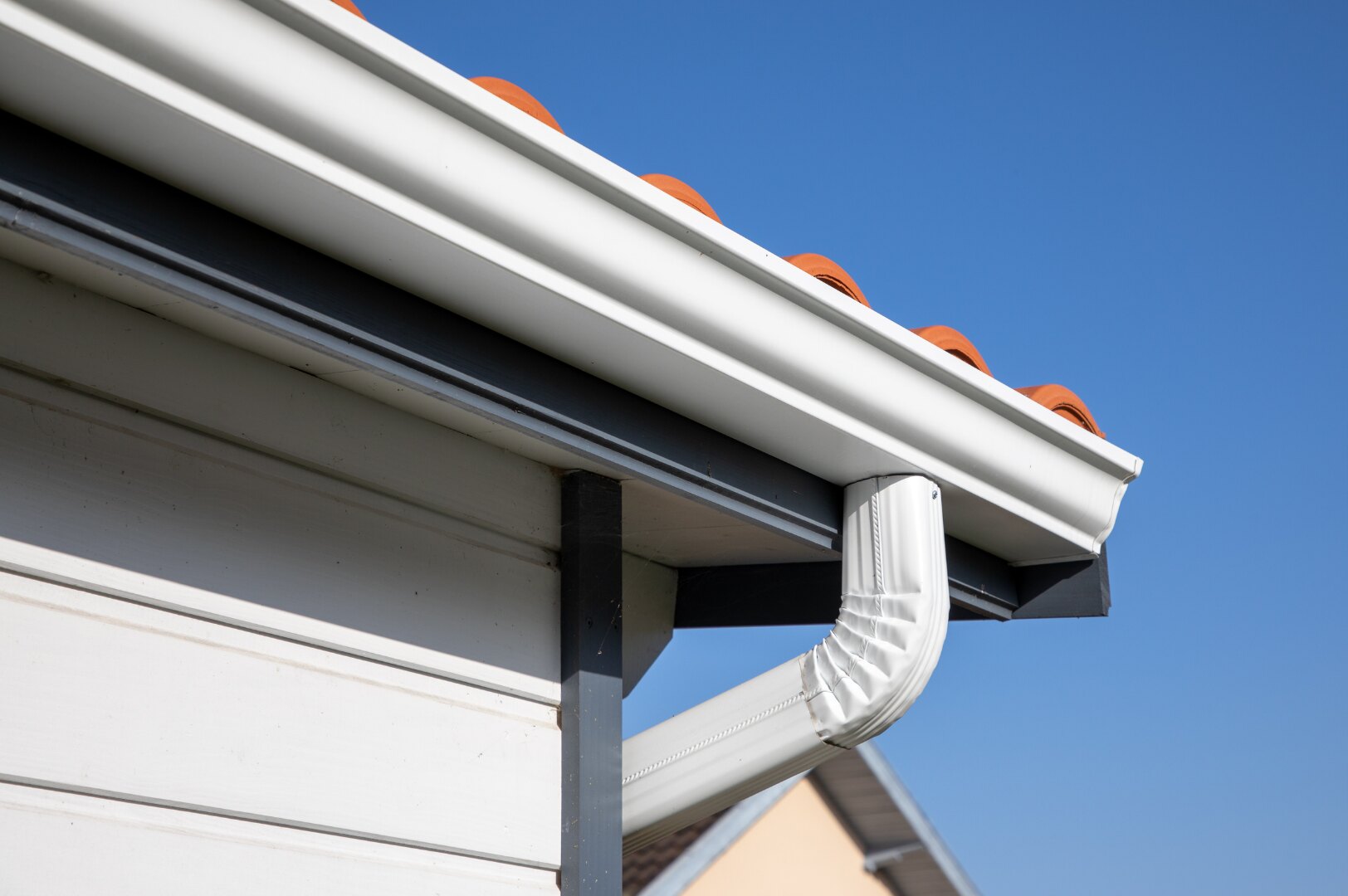 Completed white seamless gutter and downpipe against a clear blue sky