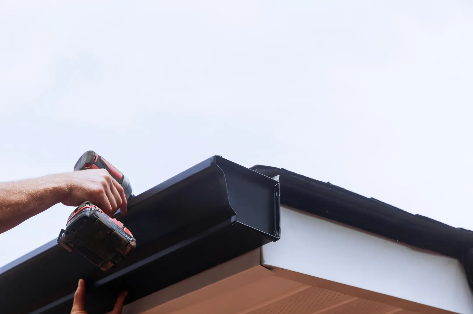Installer fastening a dark gutter at the roof edge
