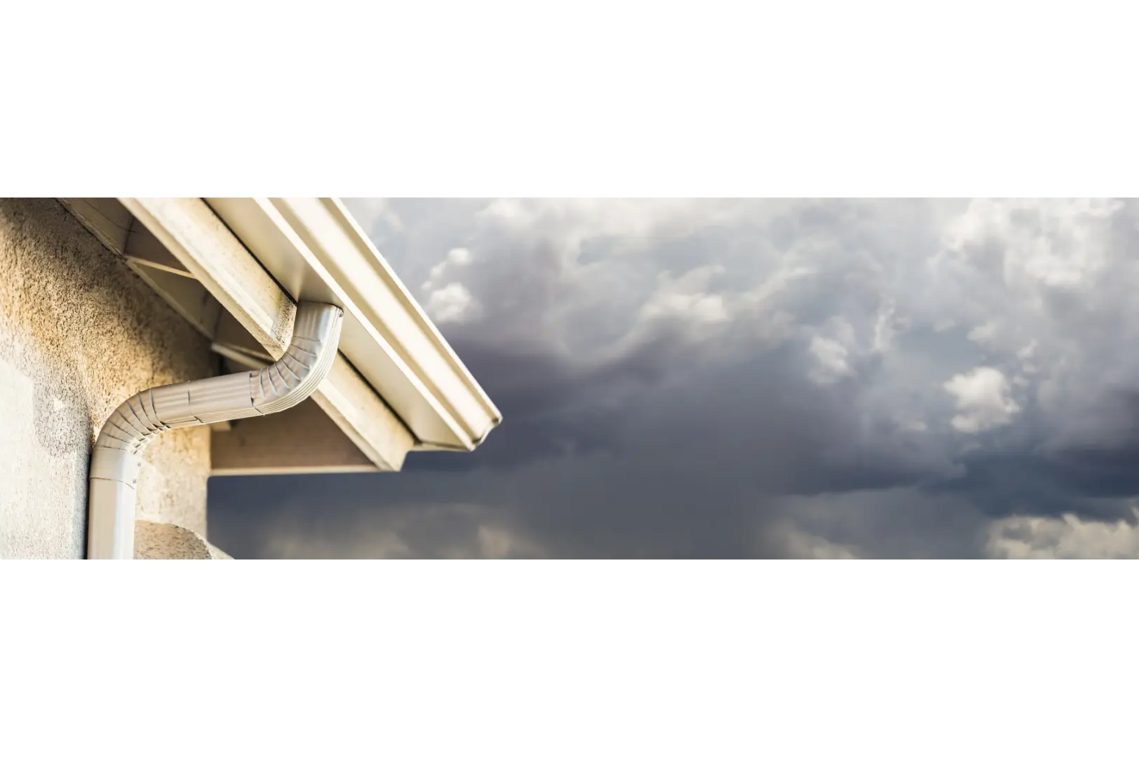 Residential gutter and downpipe beneath a cloudy sky