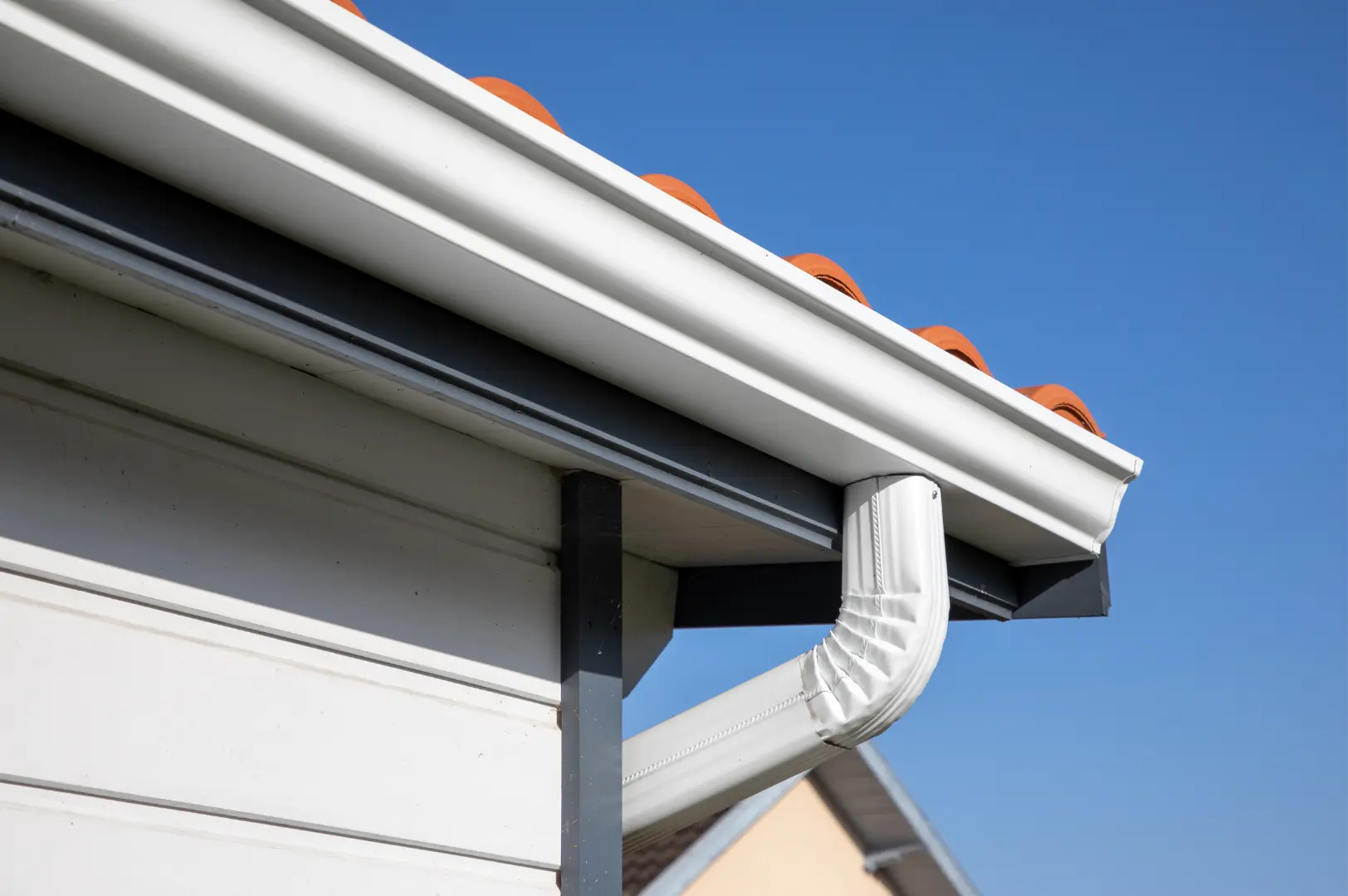 Completed white seamless gutter and downpipe against a clear blue sky