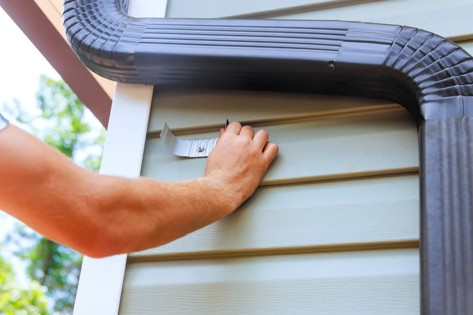 Installer checking a dark downpipe against exterior cladding
